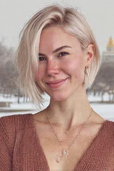 Een vrouw met een kort, asymmetrisch blond kapsel met een zijscheiding.