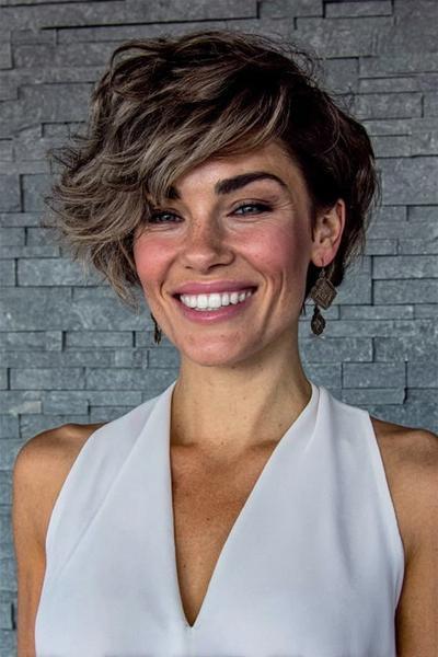 Een vrouw met kort, golvend haar in een asymmetrisch kapsel, waarbij één kant langer en volumineuzer is dan de andere.