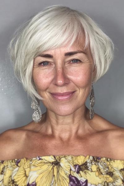 Vlotte korte kapsel voor dames van 60 plus met een asymmetrische bob en zachte, lichte pony in zilverwit haar.