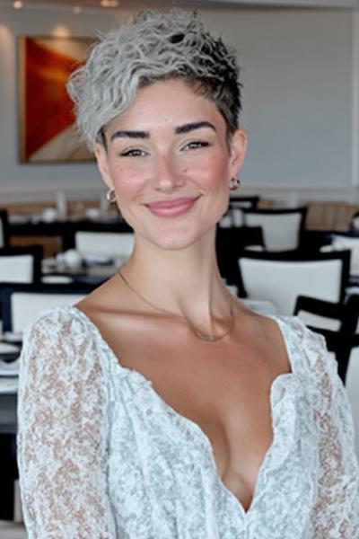 Een vrouw met een kort, golvend grijs kapsel en donkere uitgroei, gestyled in een moderne pixie cut.