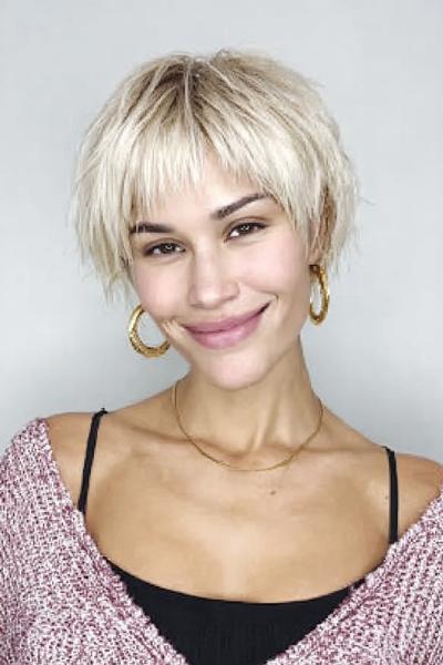 Een vrouw met een korte, blonde, getextureerde bob met pony en golvende lokken.
