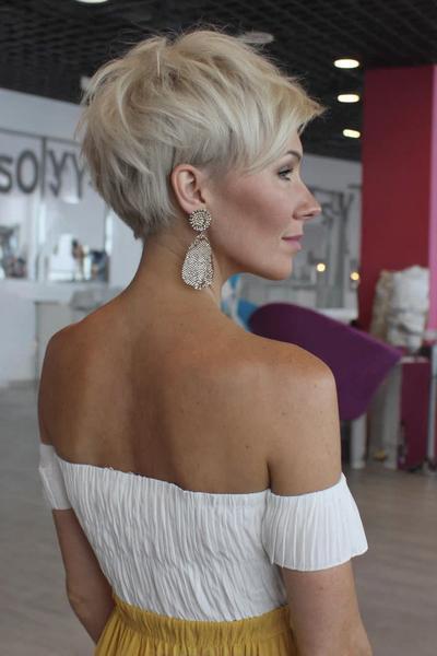 Een vrouw met kort, blond haar in een golvend en gelaagd pixiekapsel, waarbij het haar aan de achterkant korter is dan aan de bovenkant.
