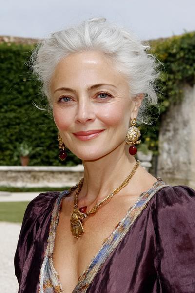 Een elegante oudere dame met witgrijs haar dat opgestoken is in een losse, volumineuze stijl.
