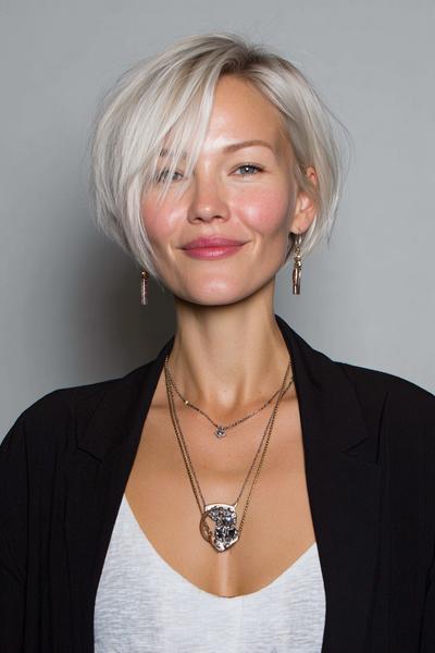 Een vrouw met een kort, asymmetrisch blond kapsel met lange lokken aan de voorkant.