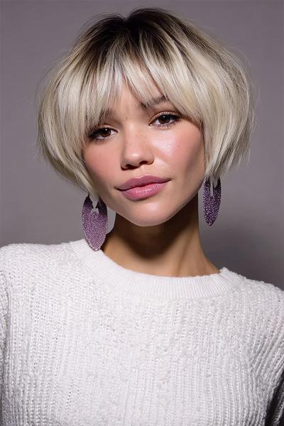 Een vrouw met een kort, blond bobkapsel met donkere aanzet en lichte, losse pony’s.