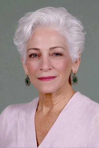 Een oudere dame met kort, golvend wit haar in een vlot en elegant kapsel.