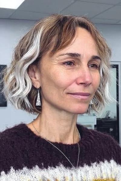 Vrouw met een kort, golvend kapsel met lichte highlights en pony, geschikt voor dames van 60 plus.