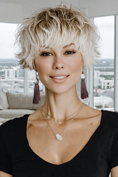 Een vrouw met een vlot, kort kapsel met golvende, blonde lokken en donkere uitgroei.