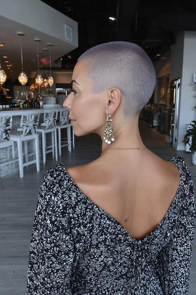 Een vrouw met zeer kort geschoren haar toont haar kapsel in een moderne, stijlvolle omgeving.