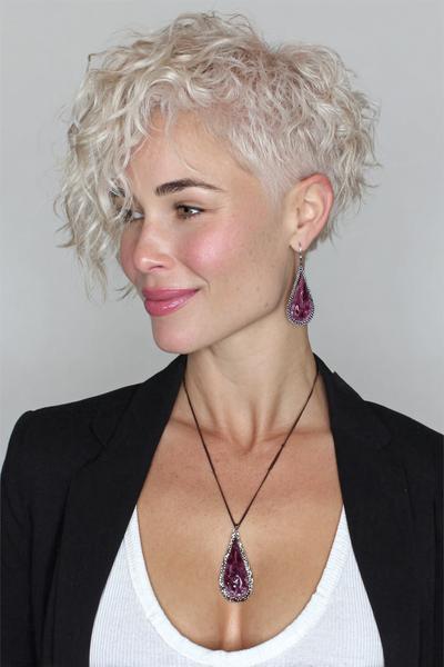 Een vrouw met een kort, asymmetrisch kapsel met blonde, golvende lokken en opgeschoren zijkanten.