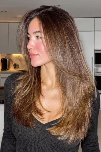 Een vrouw met lang, steil haar en subtiele lagen, met een natuurlijke bruine kleur en een midden scheiding.
