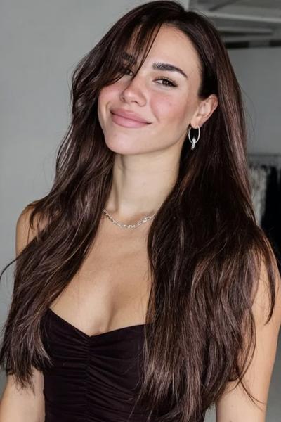 Een vrouw met lang, golvend bruin haar en lange lagen met een middenscheiding.