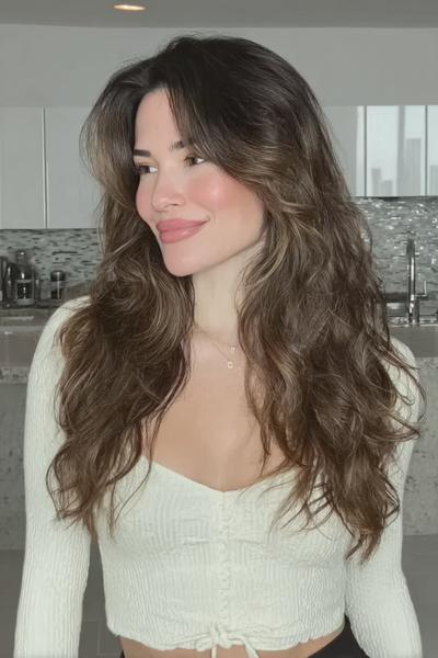 Een vrouw met lang, golvend bruin haar met veel volume en een middenscheiding.