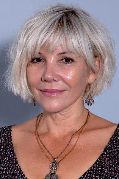 Een oudere dame met een korte, golvende bobkapsel en een pony, in een lichte blondgrijze kleur.