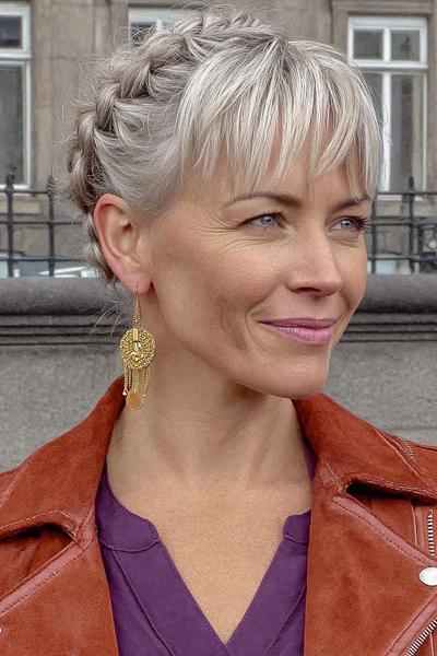 Een vrouw met grijsblond haar draagt een trendy kapsel met vlechten aan de zijkant en een pony aan de voorkant.