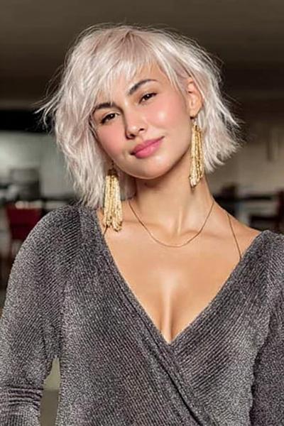 Een vrouw met een kort, golvend blond kapsel met pony en een rommelige, volumineuze uitstraling.