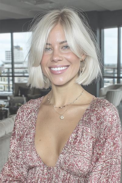 Een vrouw met een vlot, kort blond kapsel met een middenscheiding en lichte golven.