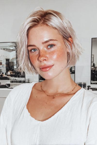 Een vrouw met een vlot, kort, blond kapsel met een lichte golving en zijscheiding.