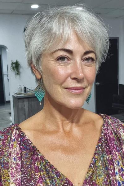 Een vlot, kort dameskapsel voor 60-plus met grijs haar, speels in laagjes geknipt en met een lichte pony naar voren gestyled.