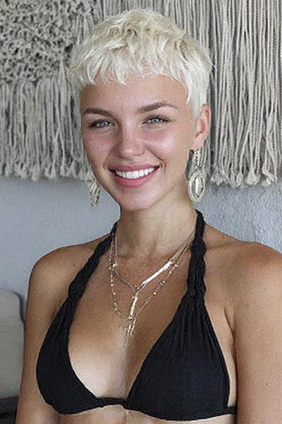 Een jonge vrouw met een kort, blond kapsel en golvende pony, gestyled in een moderne pixie cut.