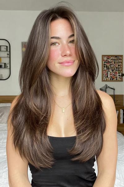 Een vrouw met lang, dik haar dat in lagen is geknipt en een middenscheiding heeft.