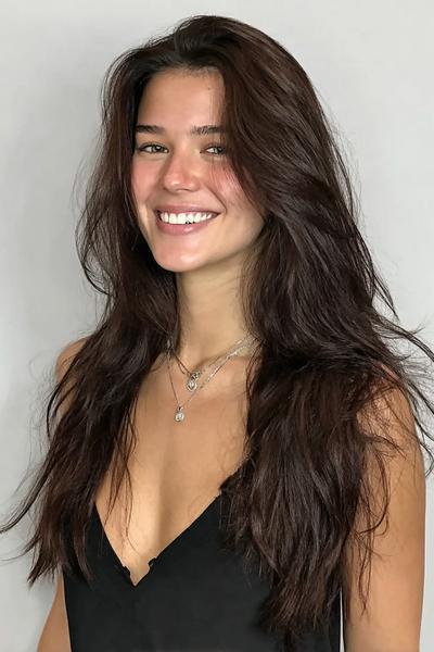 Een vrouw met lang, dik, golvend donkerbruin haar en een natuurlijke, volumineuze look.