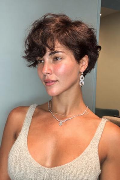 Een vrouw met een vlot, kort kapsel met golvend, donkerbruin haar dat speels en volumineus is gestyled.