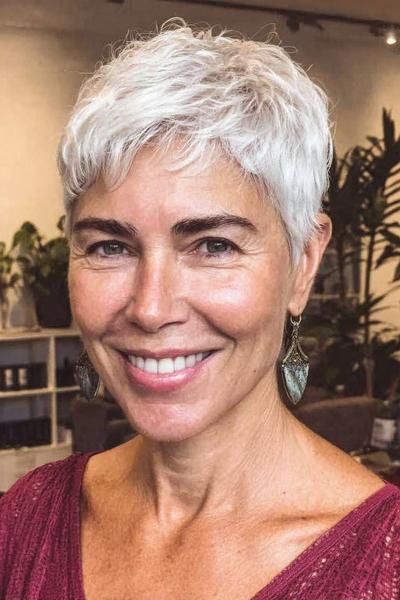 Vlotte korte kapsel met zachte, golvende, witte lokken en een speelse pony, geschikt voor vrouwen van 60 plus.