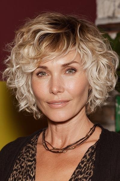 Een vrouw met een kort, golvend kapsel met blonde highlights en donkerdere uitgroei.