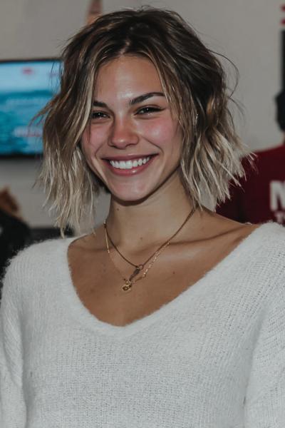 Een vrouw met een kort, warrig bobkapsel met licht golvend haar en blonde highlights.