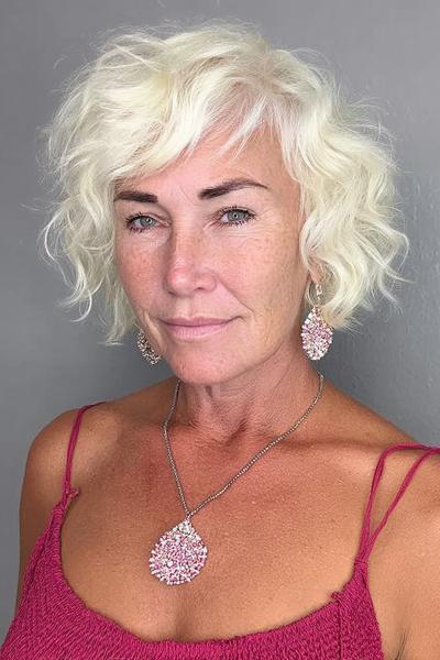 Een vrouw met kort, golvend wit haar en een zijscheiding, gestyled in een speelse en volumineuze look.