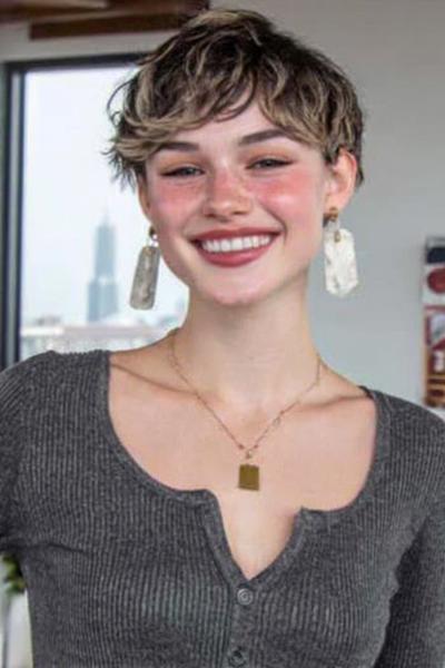 Een jonge vrouw met een vlot, kort kapsel met golvende, licht getoupeerde lokken en een speelse, warrige look.