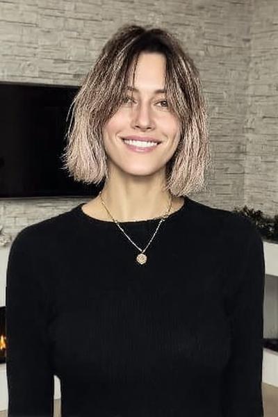 Een vrouw met een kort, golvend bobkapsel met een middenscheiding en lichte highlights.