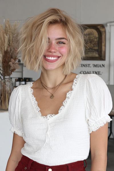 Een vrouw met een vlot, kort kapsel met rommelige, blonde lokken en een zijscheiding.