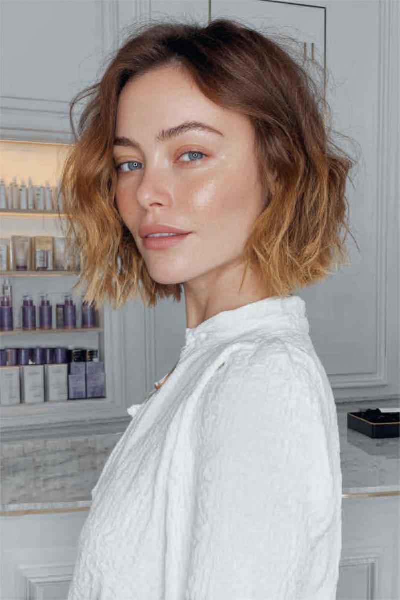 Een vrouw met een kort, golvend bobkapsel met een subtiele ombre van donkerblond naar lichtblond.