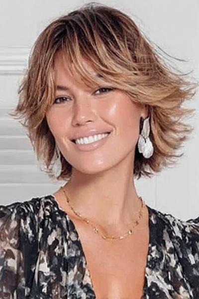 Een vrouw met kort, gelaagd haar dat speels en volumineus is gestyled met lichte highlights.