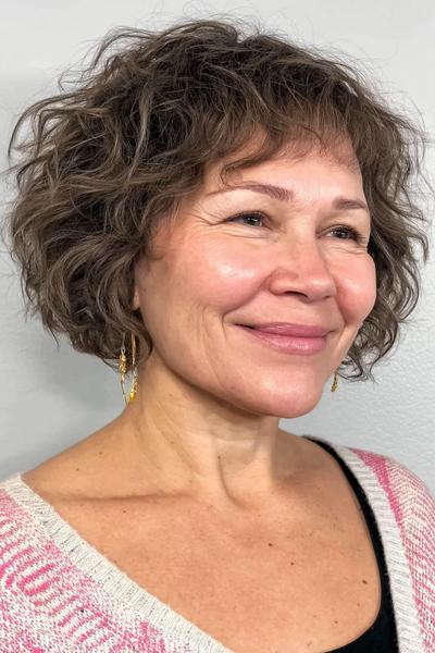 Vrouw met kort, golvend haar in een vlot kapsel dat volume en speelsheid geeft, geschikt voor vrouwen boven de 60 jaar.