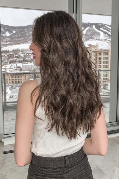 Een vrouw met lang, golvend bruin haar draagt een wit mouwloos topje en staat met haar rug naar de camera.