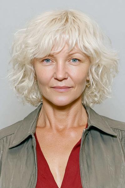 Een oudere dame met een kort, golvend, lichtblond kapsel en een zachte pony.