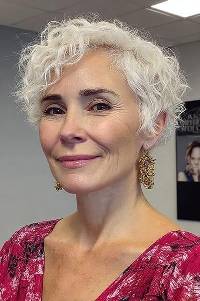 Een vlotte korte kapsel voor dames van 60 plus met natuurlijke witte, krullende haren en een frisse, speelse uitstraling.