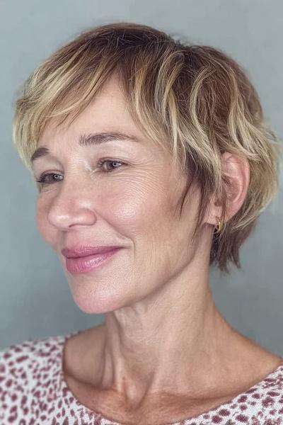 Een vrouw met een kort, gelaagd kapsel met zachte, blonde highlights en zijwaartse pony, geschikt voor dames van 60 plus.