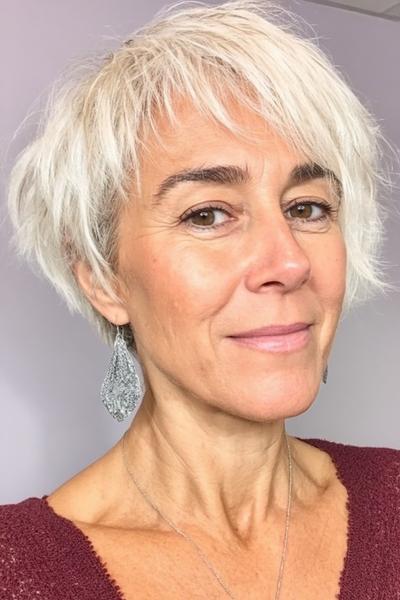 Een vrouw met een vlot, kort en gelaagd grijs kapsel met warrige pony, geschikt voor dames van 60 plus.