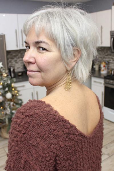 Een vrouw met kort, vlot grijs haar in een speelse, gelaagde coupe geschikt voor dames van 60 plus.