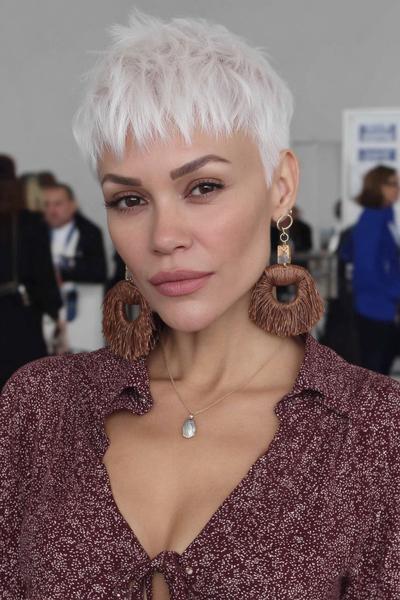 Een vrouw met een trendy, kort platina blond kapsel met warrige, gelaagde lokken en een pony.