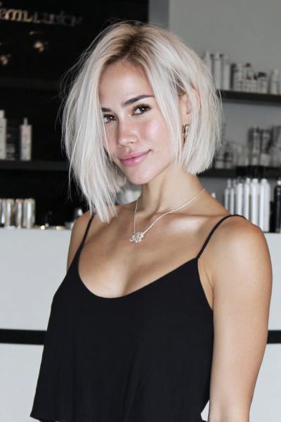 Een jonge vrouw met een modieuze, asymmetrische blonde bobkapsel met zijscheiding en steil haar.