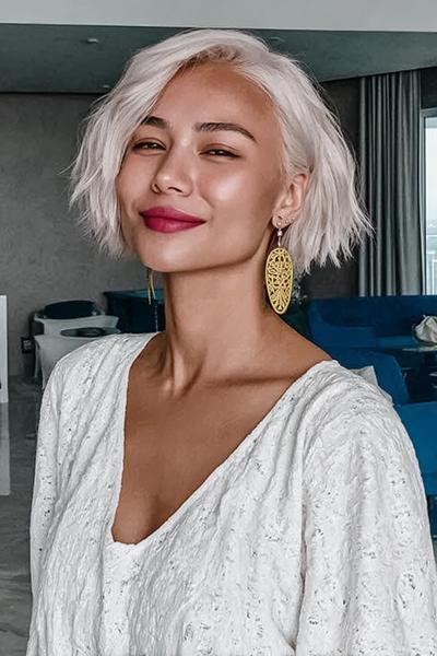 Een vrouw met een kort, golvend, platinablond kapsel en een zijscheiding.