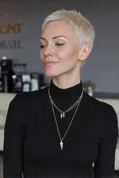 Een vrouw met een kort, blond pixie kapsel en een strakke zwarte coltrui.