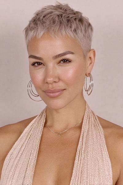 Een vrouw met een kort, platina blond kapsel in een moderne pixie cut met getextureerde lagen en korte pony.