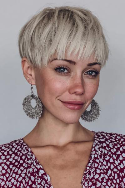 Een vrouw met een kort, blond kapsel met een volle pony en zachte, gelaagde textuur.