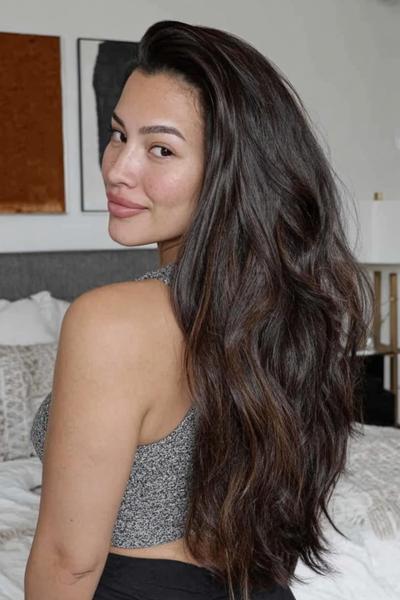 Een vrouw met lang, golvend donkerbruin haar dat los over haar schouders valt.